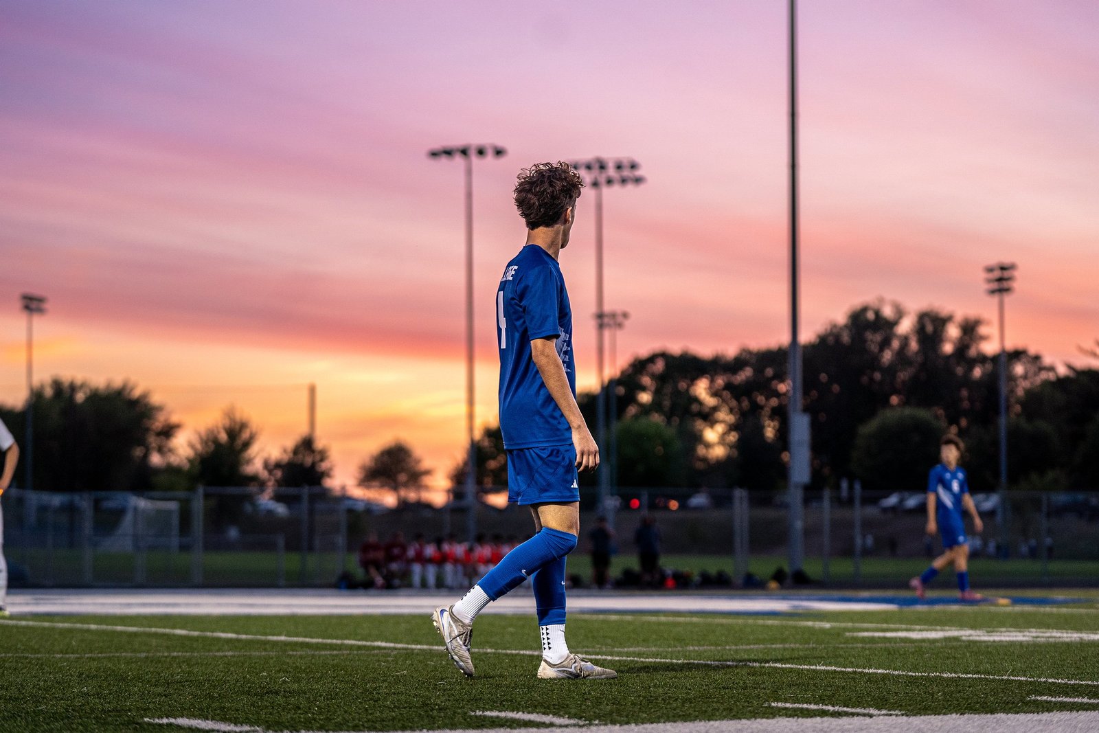 Soccer player walking the field under a pink and orange sunset