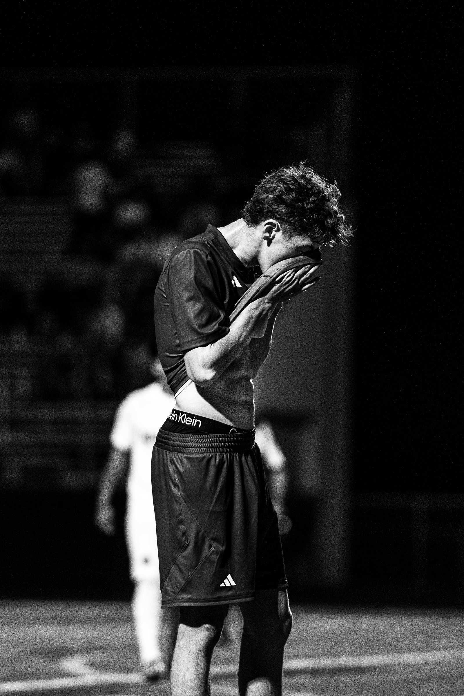 Black and white of a soccer player covering his face after a night game